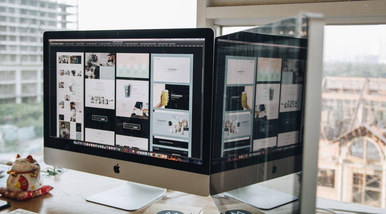 heros-img Dual monitors on a desk, showcasing web design in a modern office setting.